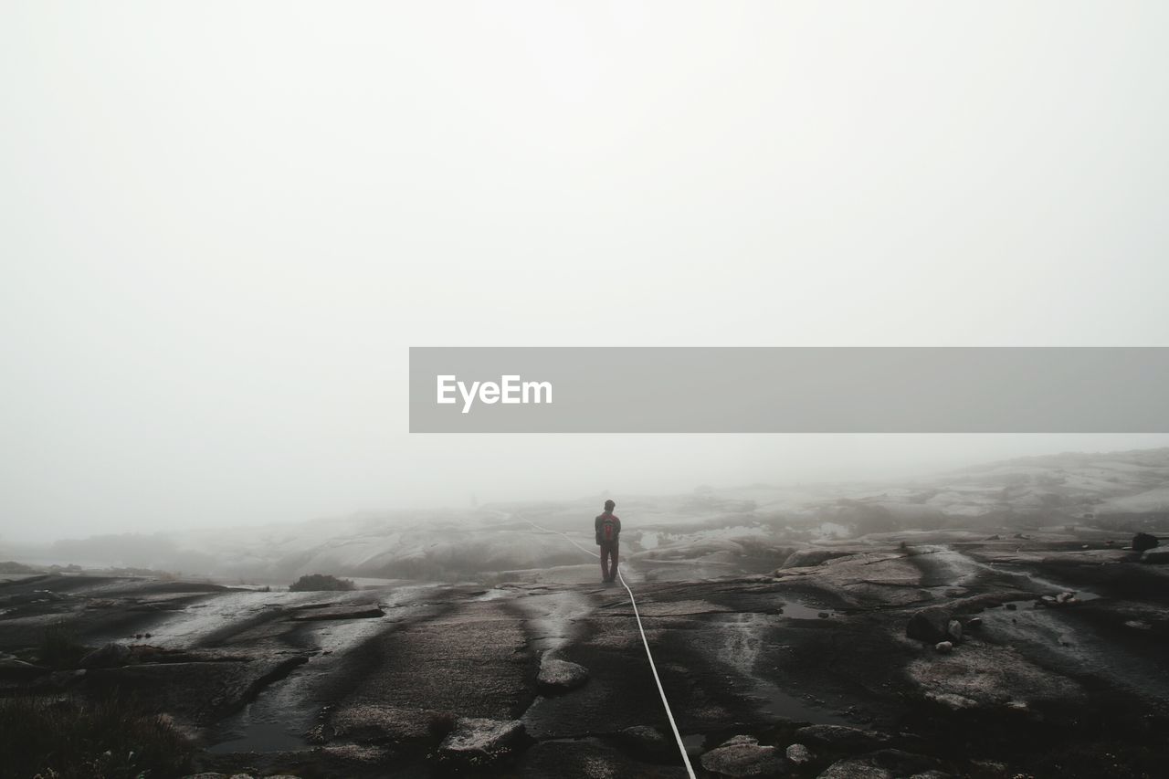 Rear view of man standing on landscape in foggy weather