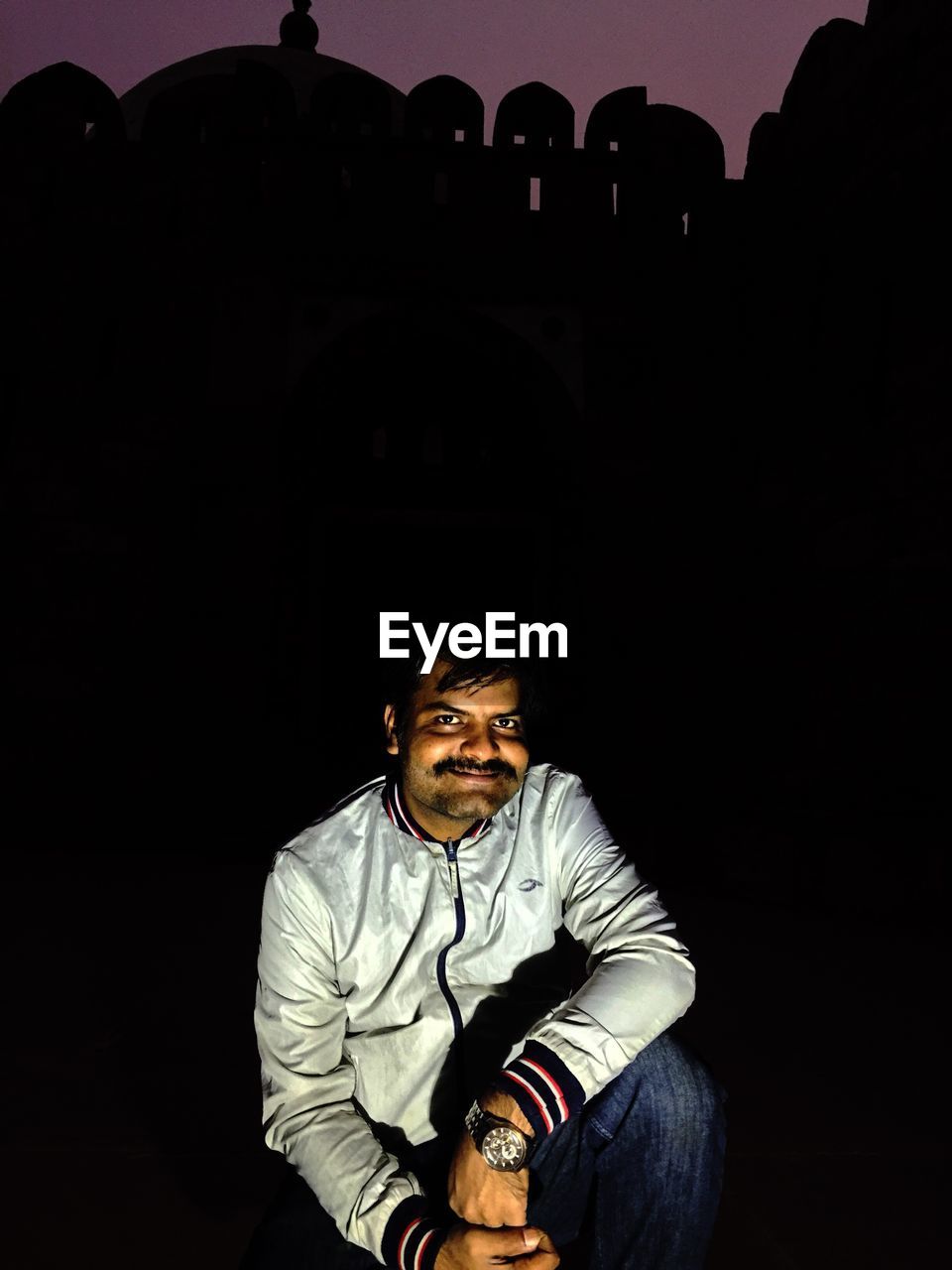 PORTRAIT OF MAN SITTING AGAINST BLACK BACKGROUND AT NIGHT