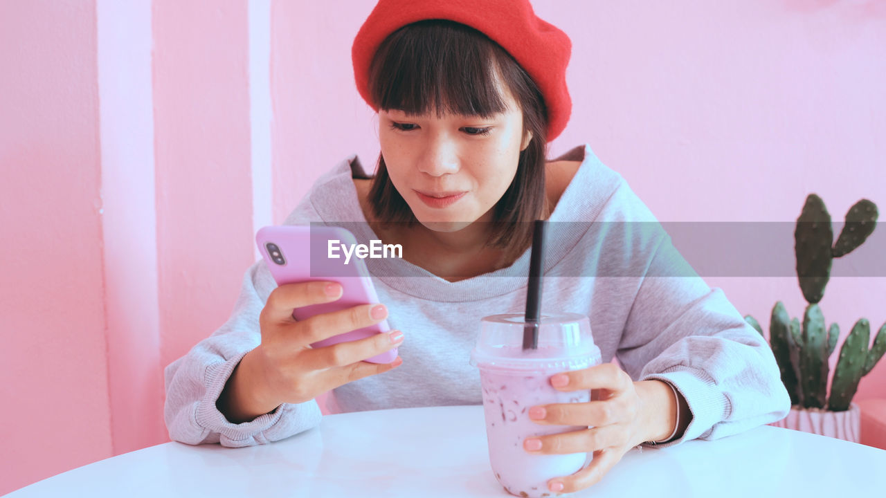 Young woman using mobile phone while having drink at table