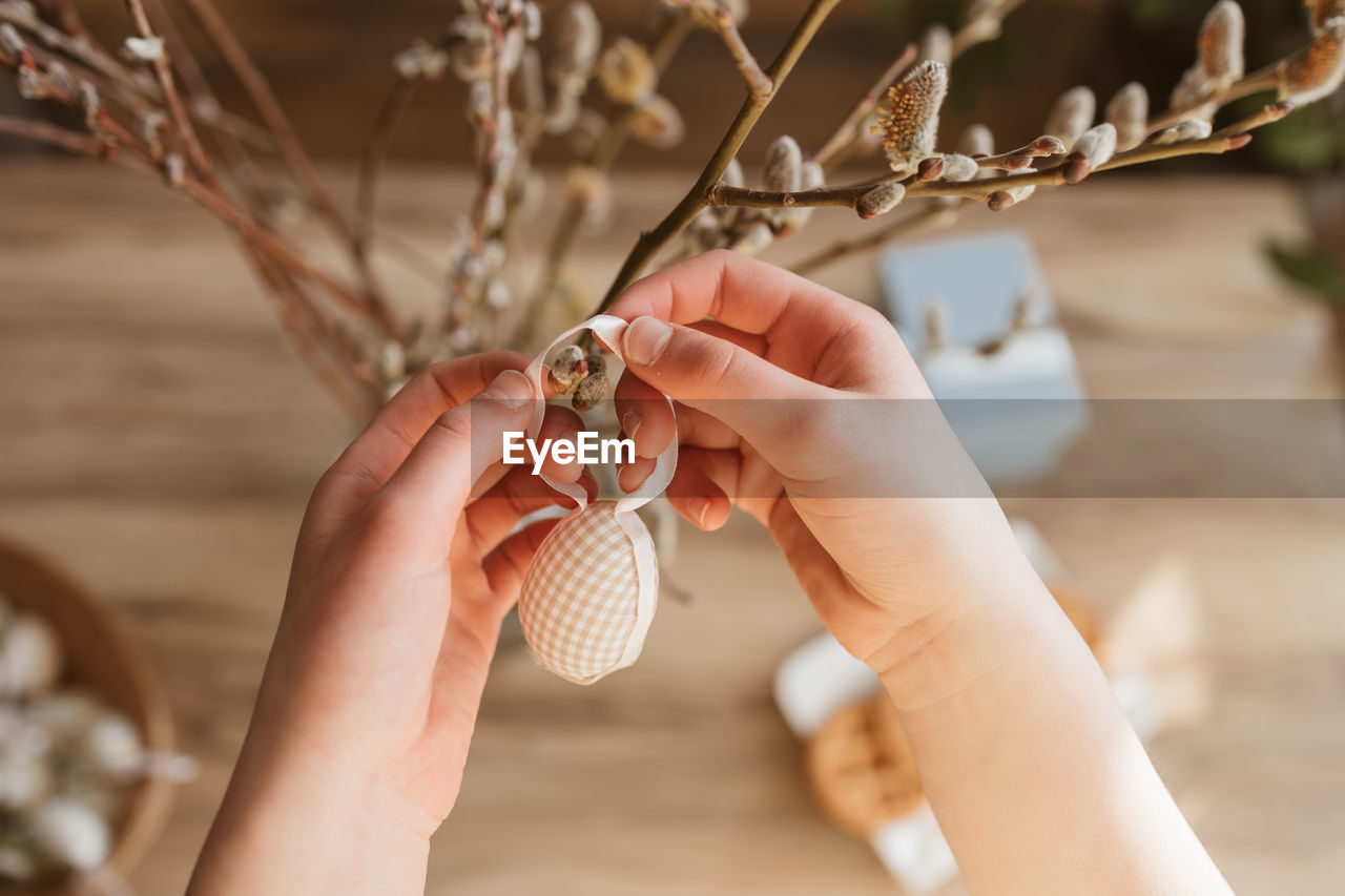  girl's hands hanging a decorative easter egg on a willow branch at home. decorating home for easter