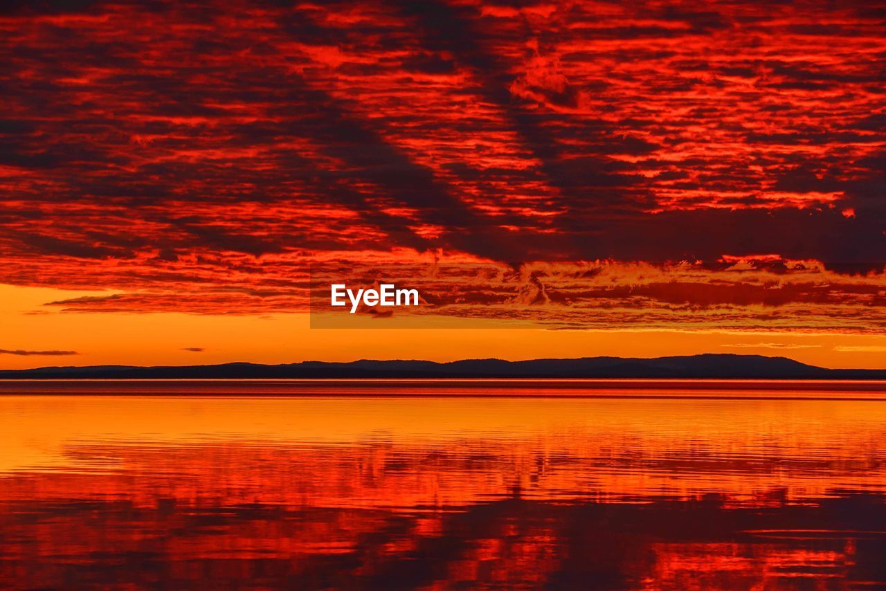 Scenic view of lake against cloudy sky during sunset