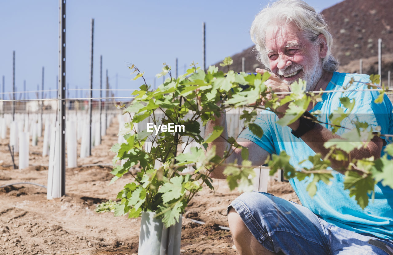 Close-up of smiling senior man crouching by plant outdoors