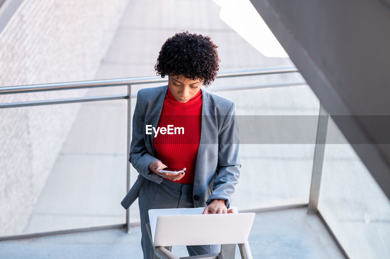 Young african-american businesswoman using her phone and laptop in a business building