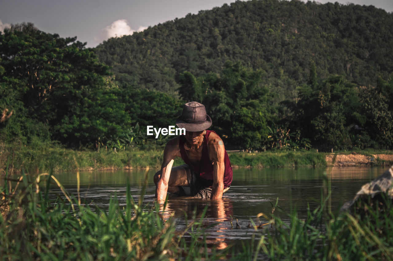 Man crouching in lake against mountains