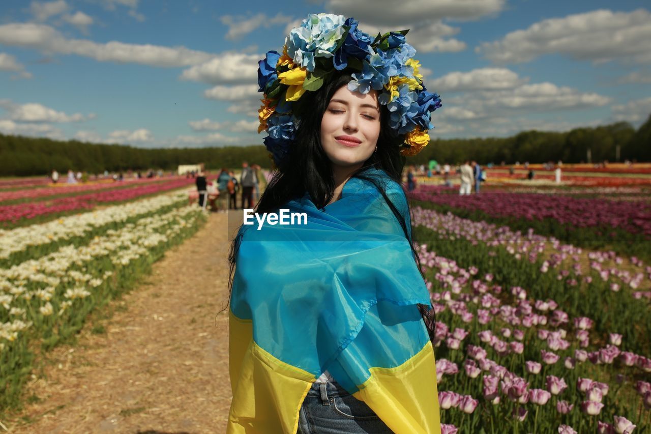 Portrait of young woman standing on field with the ukrainian flag