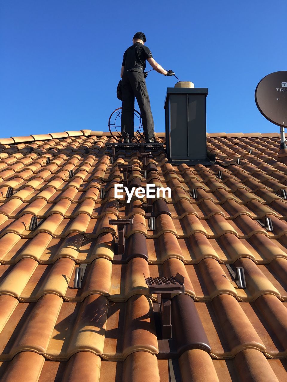 Low angle view of man standing on roof and cleaning the chimney 