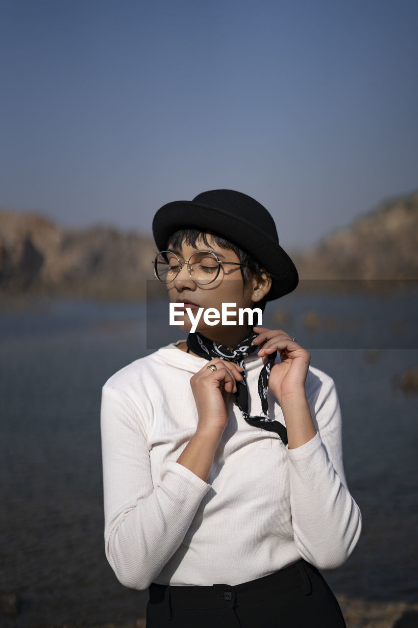 Young woman wearing hat standing against lake