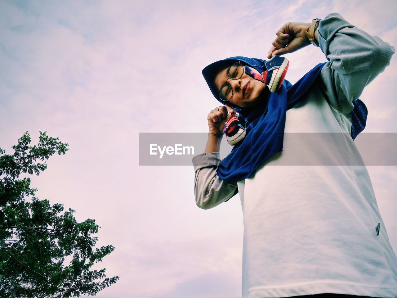 Low angle view portrait of woman holding small shoes standing against sky