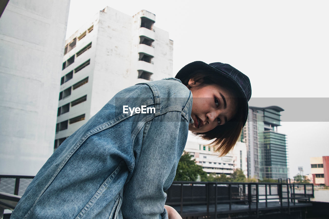 Portrait of woman standing by railing against buildings in city