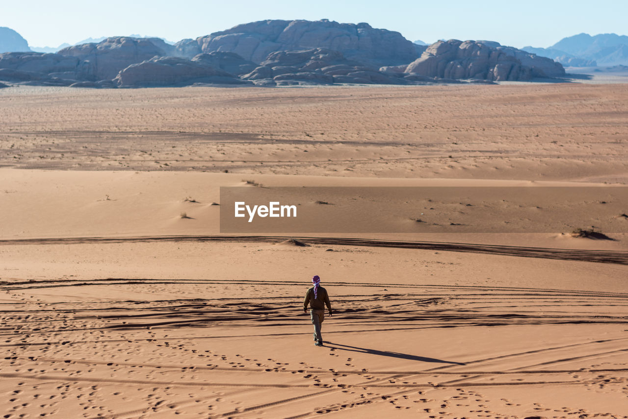 Full length rear view of man walking on desert