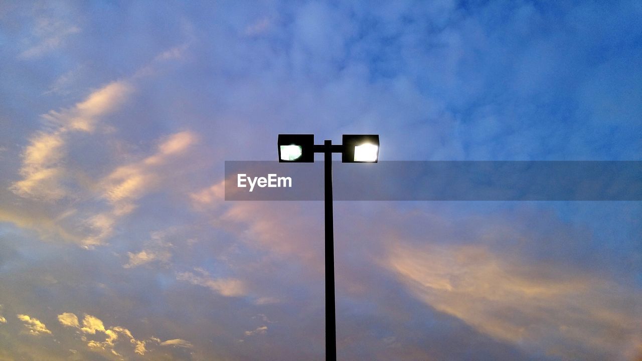 Low angle view of illuminated street light against cloudy sky at sunset