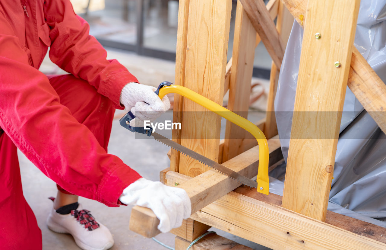 A worker is sawing wood to assemble a crate for moving an industrial machine. a woman in red