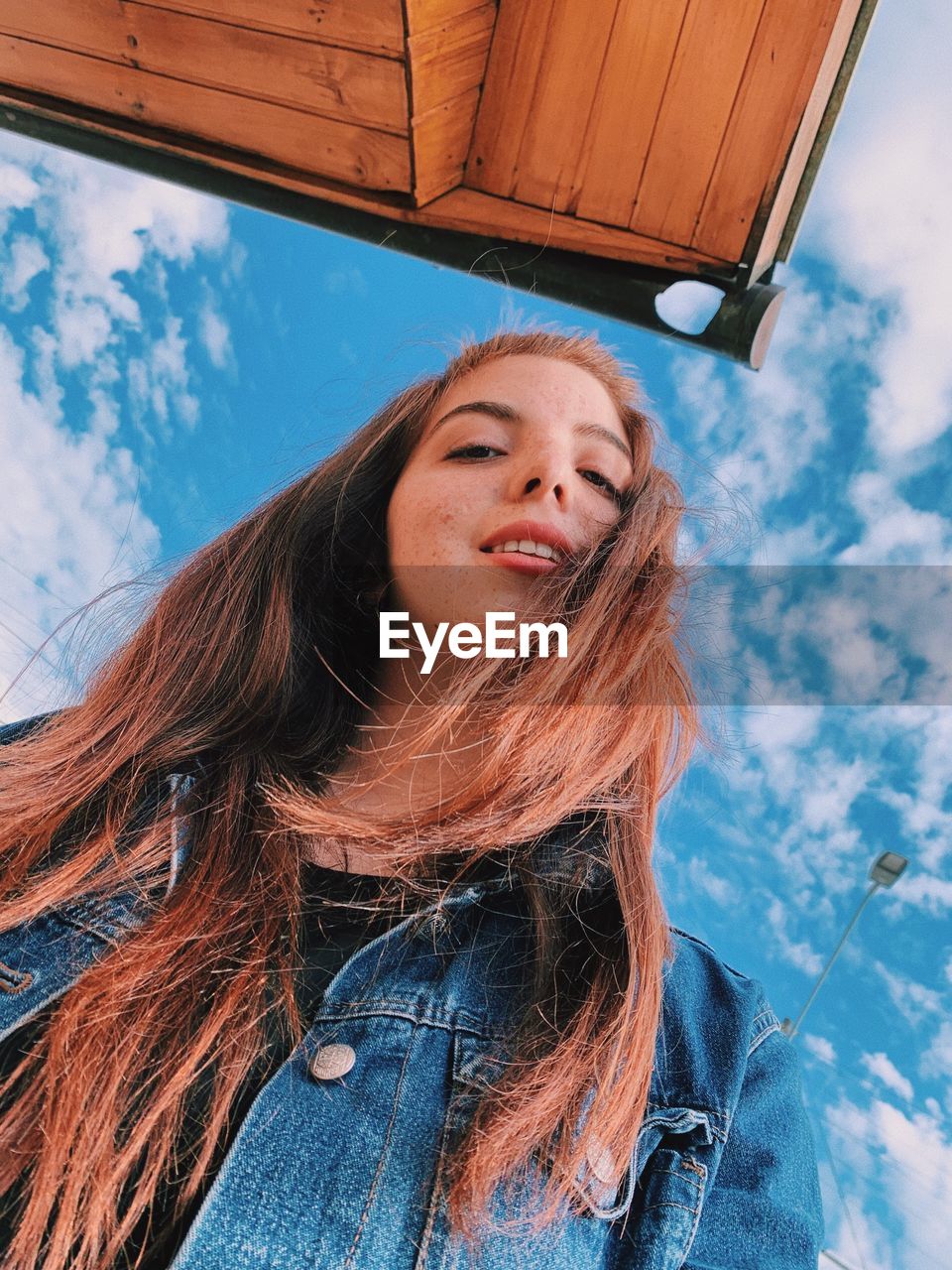 Low angle portrait of smiling young woman standing against sky