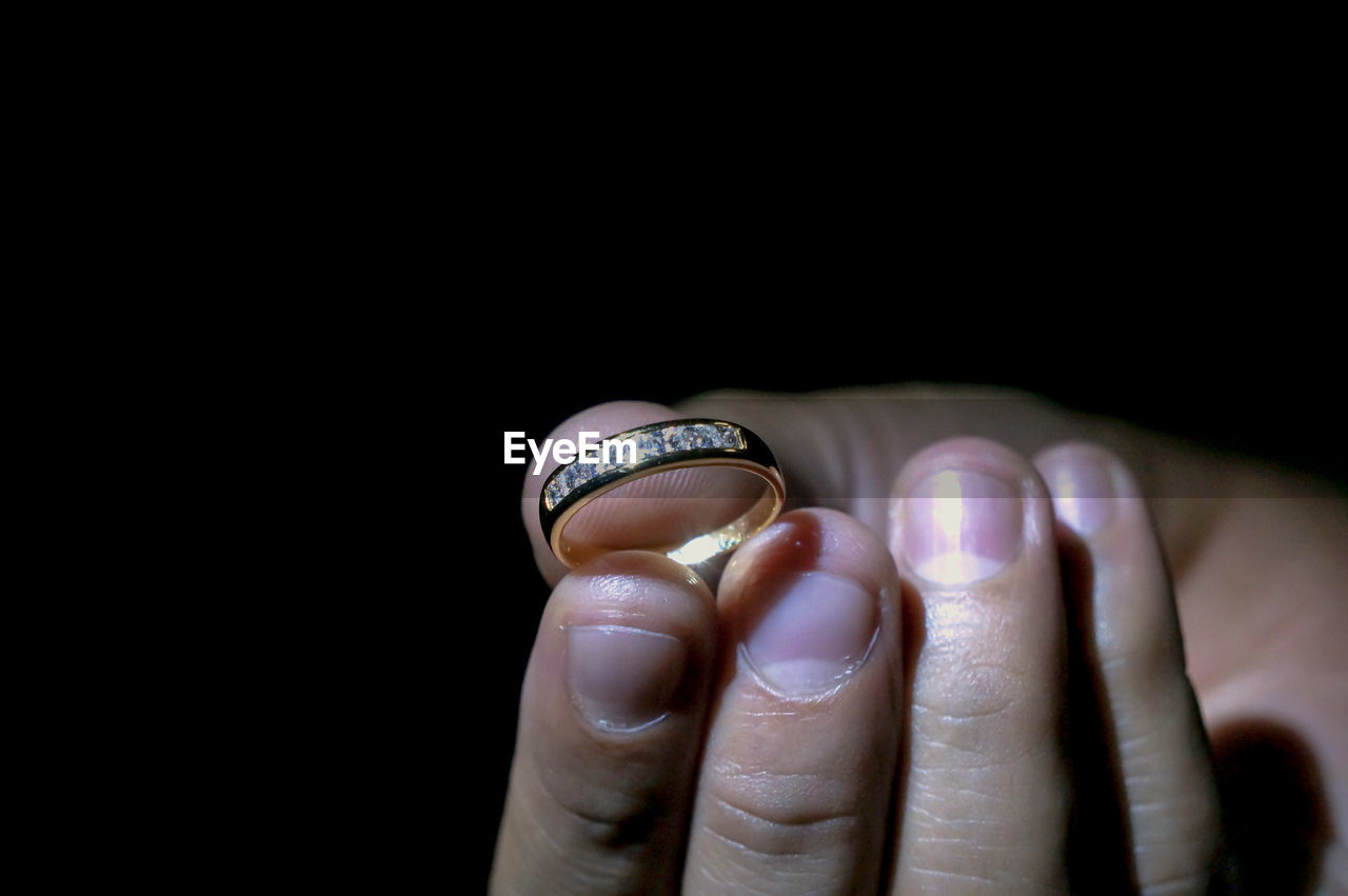 Cropped hand of woman holding ring against black background