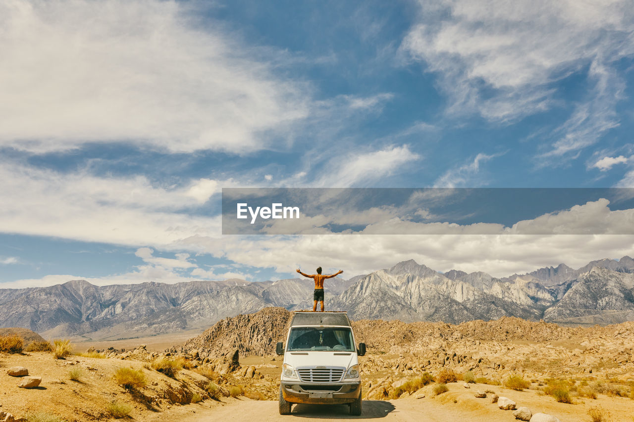 Young man on roof of camper van with open arms in northern california.