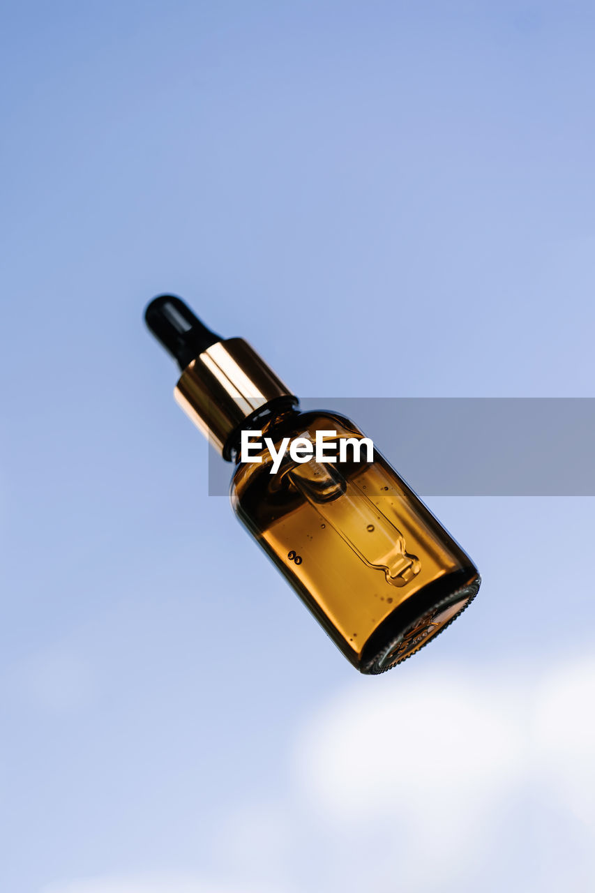 A brown bottle of serum against the sky.