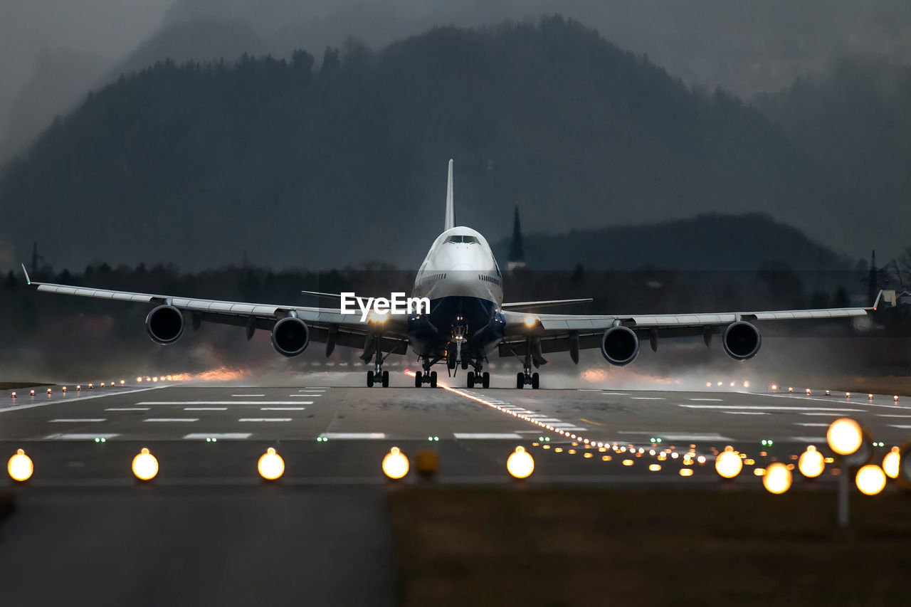 Airplane on illuminated runway against mountain range