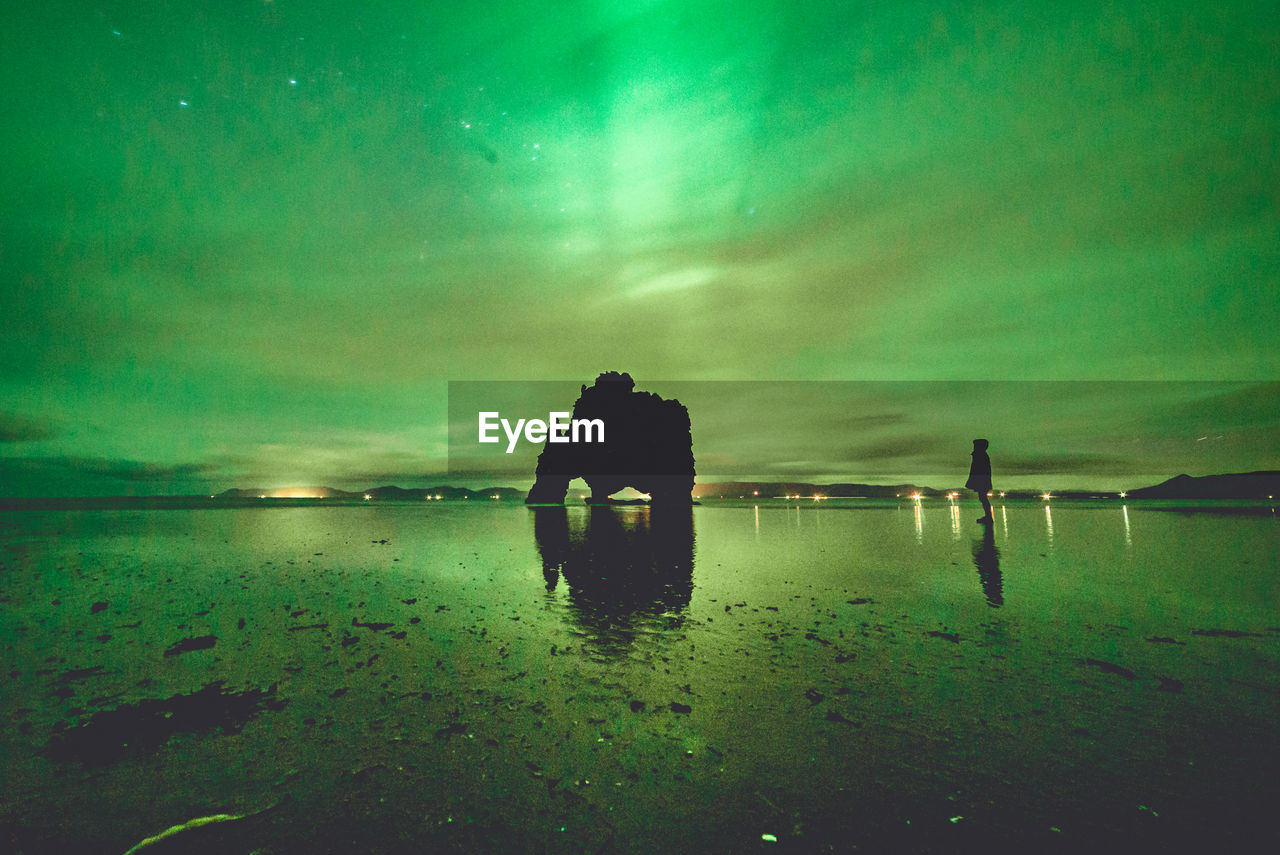 Silhouette man at beach against green sky at night