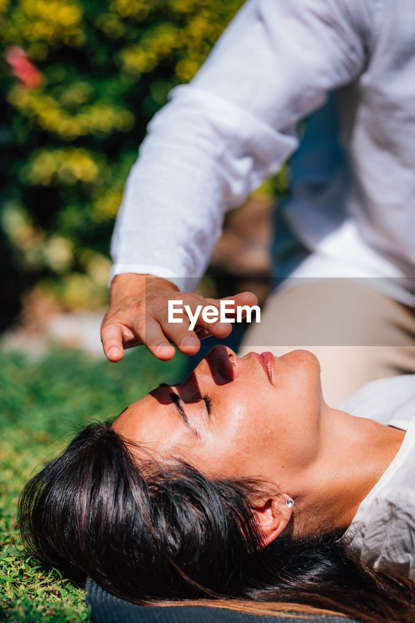 Close-up image of relaxed woman lying with her eyes closed and having reiki healing treatment