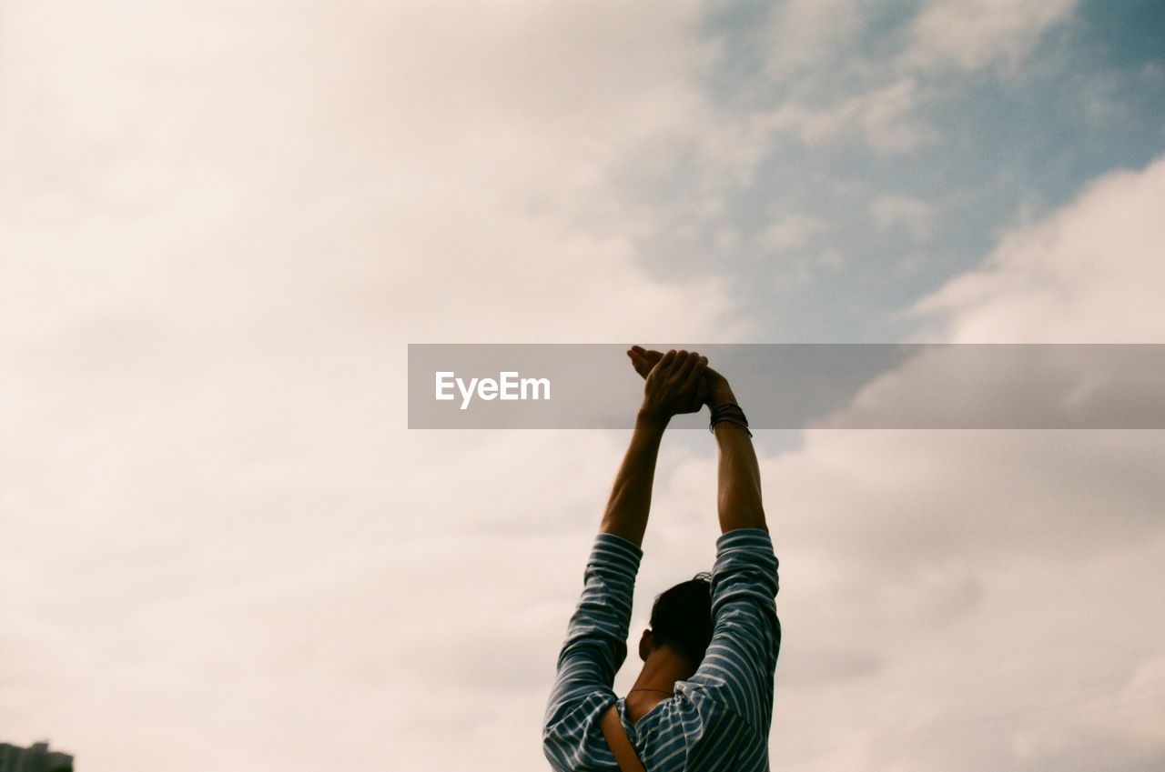 Rear view of man with arms raised against cloudy sky