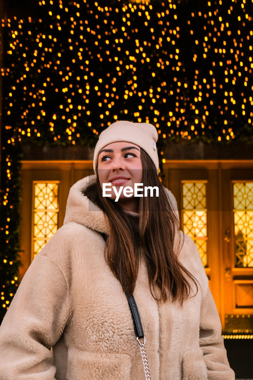 Young woman looking away while standing against christmas decoration