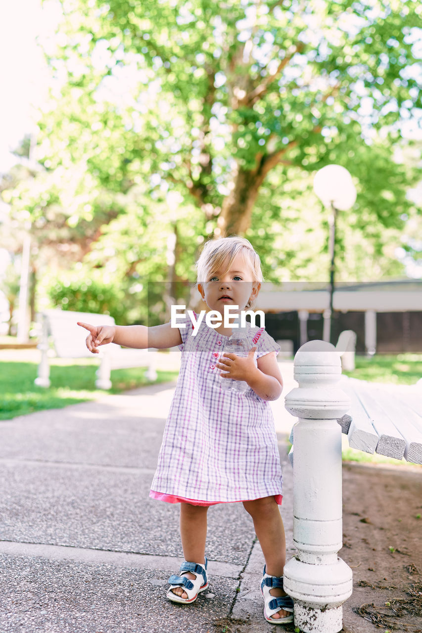 FULL LENGTH OF CUTE GIRL STANDING AGAINST BLURRED BACKGROUND