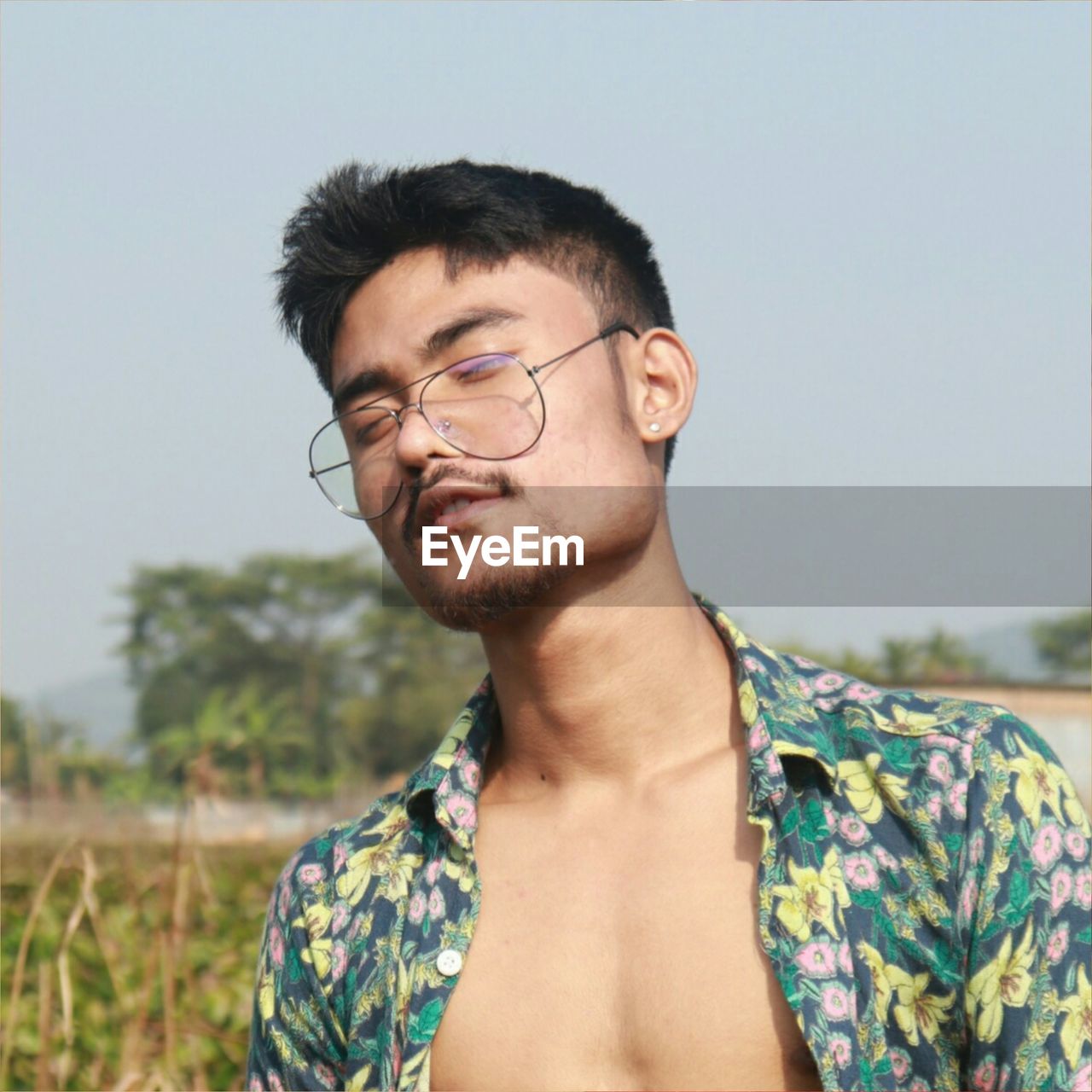 one person, glasses, portrait, adult, young adult, eyeglasses, headshot, hairstyle, men, beard, photo shoot, nature, sky, front view, person, day, casual clothing, facial hair, human hair, black hair, leisure activity, focus on foreground, waist up, smiling, teenager, spring, looking, land, outdoors, emotion, standing, pattern, fashion, lifestyles, copy space, relaxation, human face, clothing, happiness, summer, tattoo, looking at camera, rural scene, landscape, cool attitude, close-up, clear sky, portrait photography, plant, contemplation, sunny, eyes closed