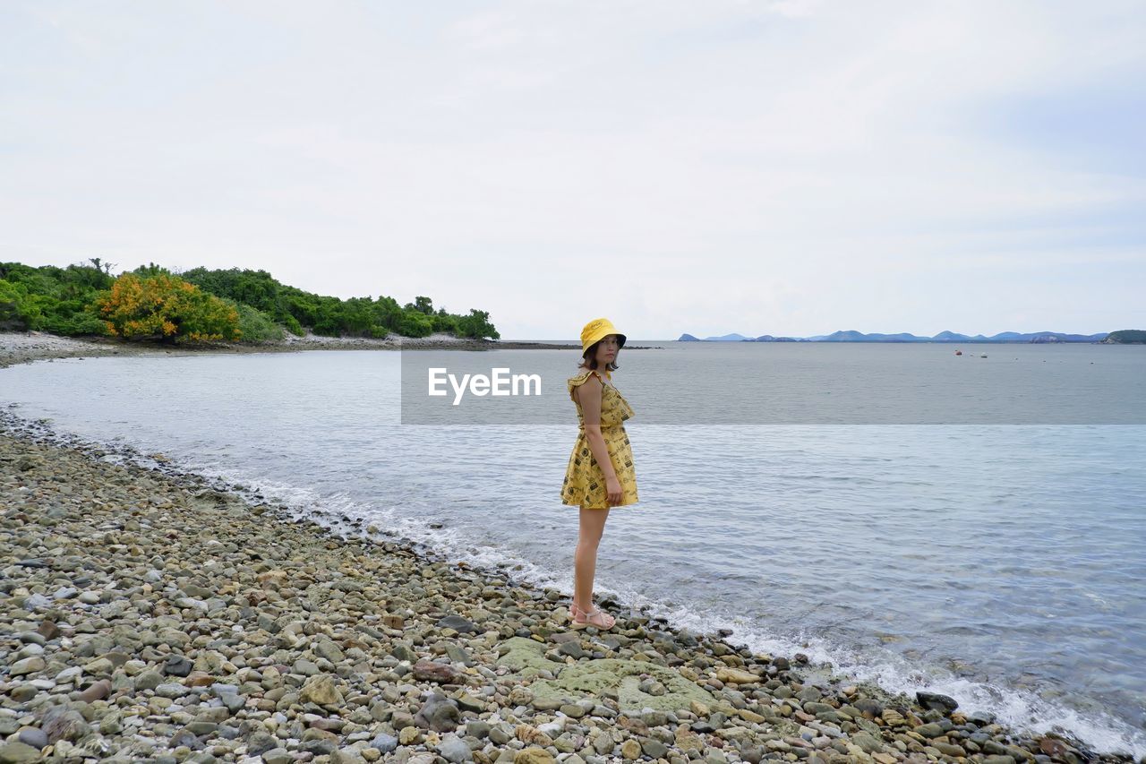 WOMAN STANDING ON BEACH AGAINST SKY