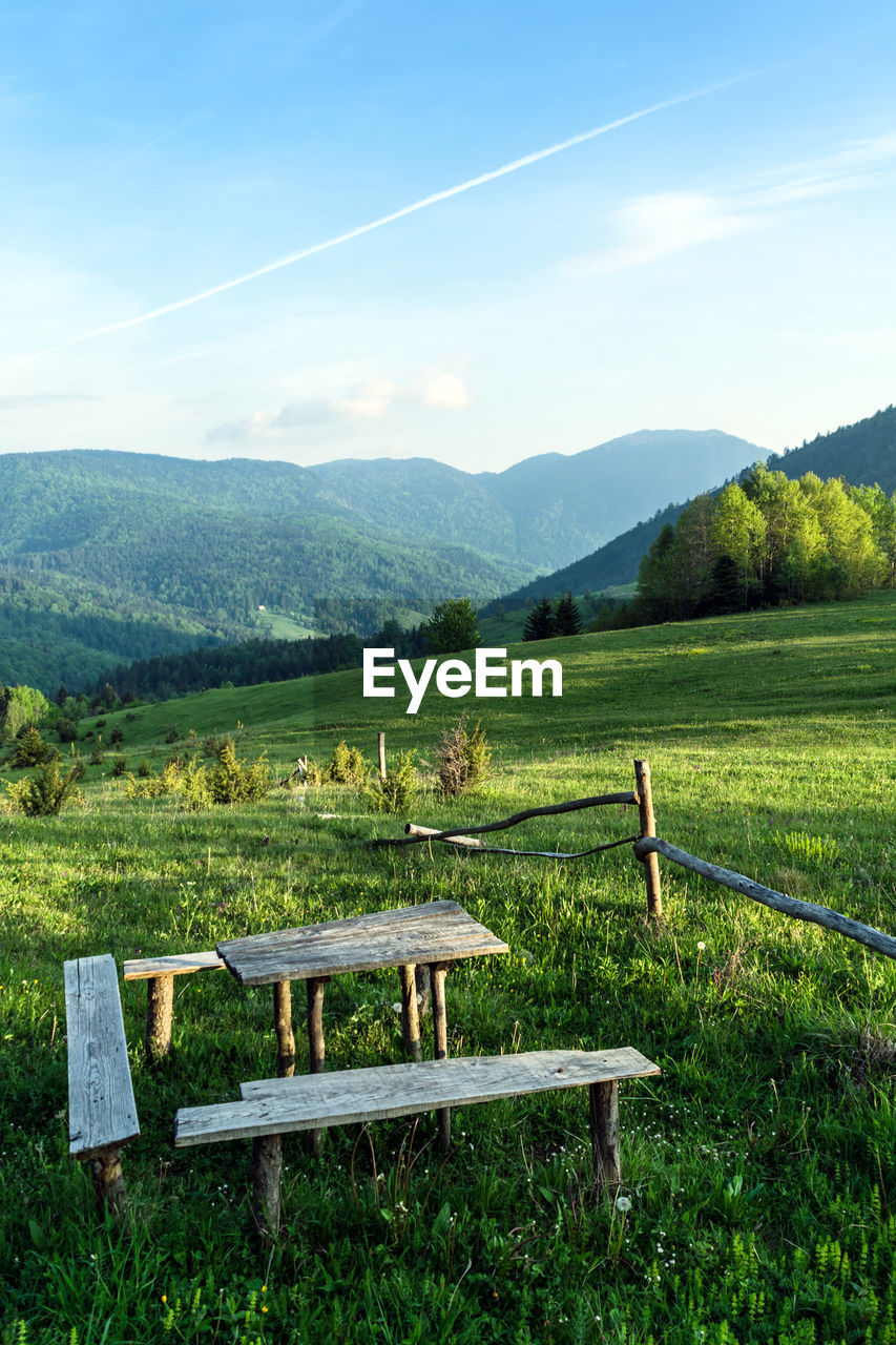 Scenic view of a wooden bench with table on a field against sky