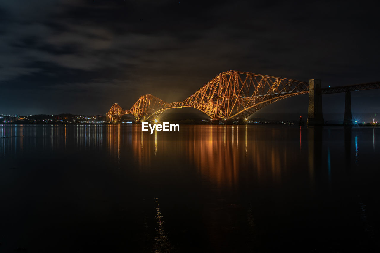 Illuminated bridge over river against sky at night