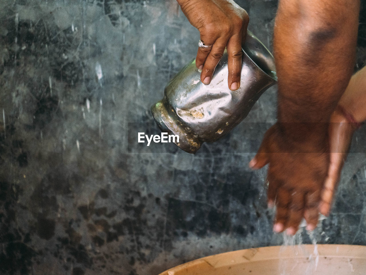 Cropped image of man pouring water on male friend hands