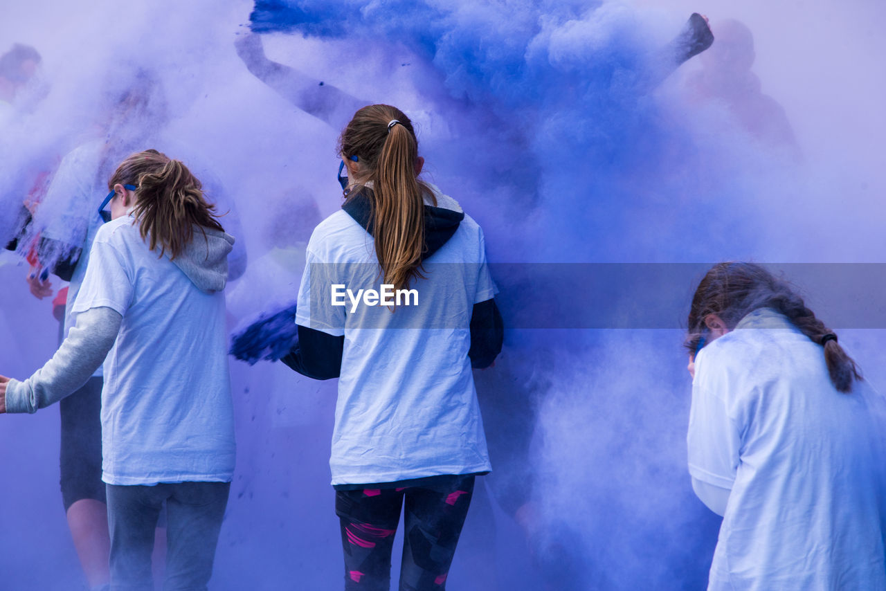 Rear view of teenage girls playing in blue powder paint