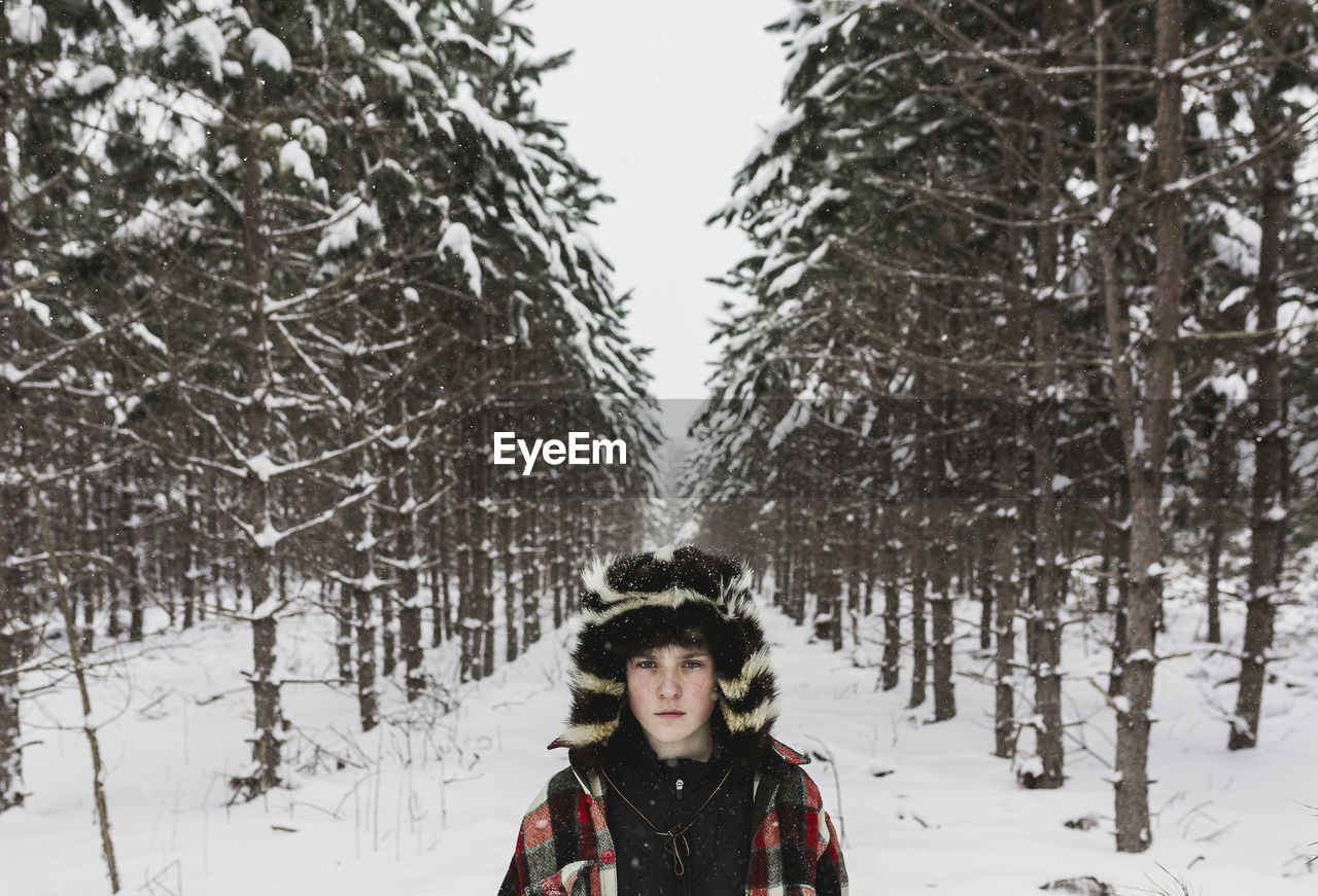 Portrait of confident teenage boy wearing warm clothing while standing in forest during winter