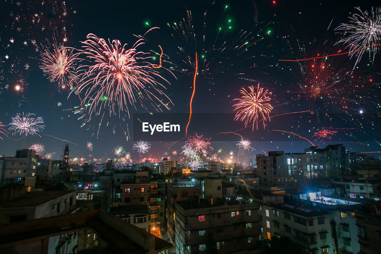 Firework display in city against sky at night