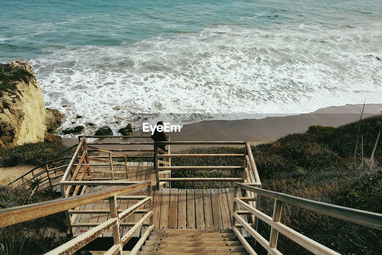 High angle view of man standing on wooden staircase at beach