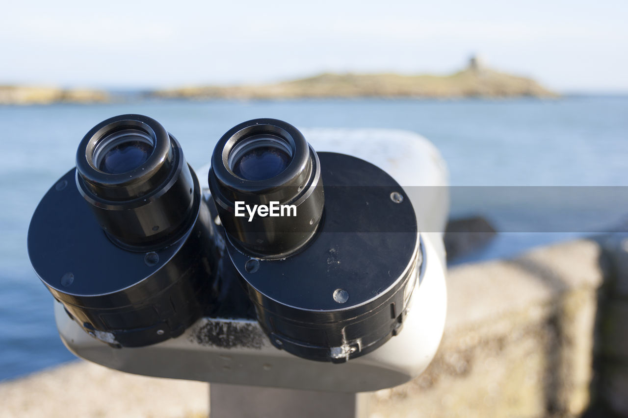 Close-up of coin-operated binoculars at beach against sky
