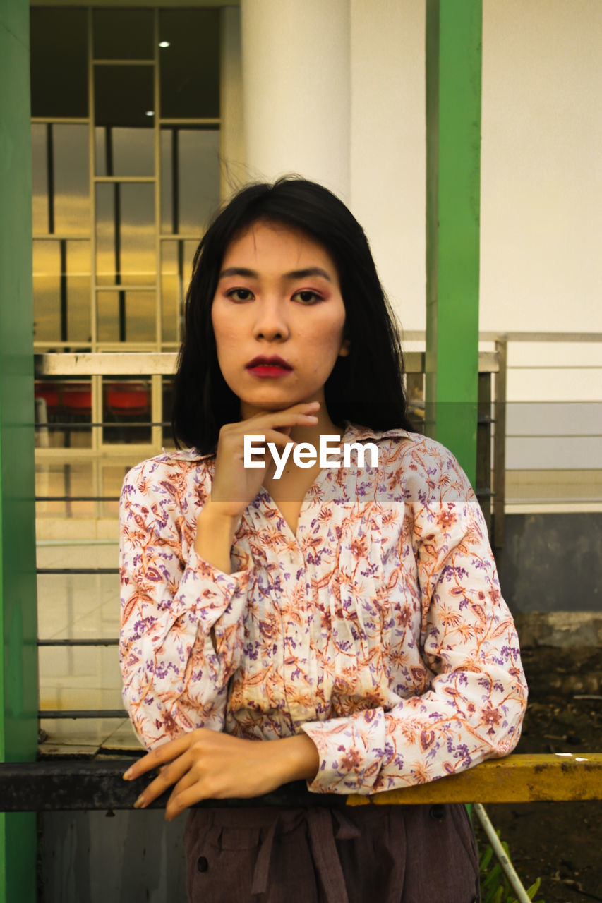 PORTRAIT OF BEAUTIFUL YOUNG WOMAN STANDING AGAINST BUILDING