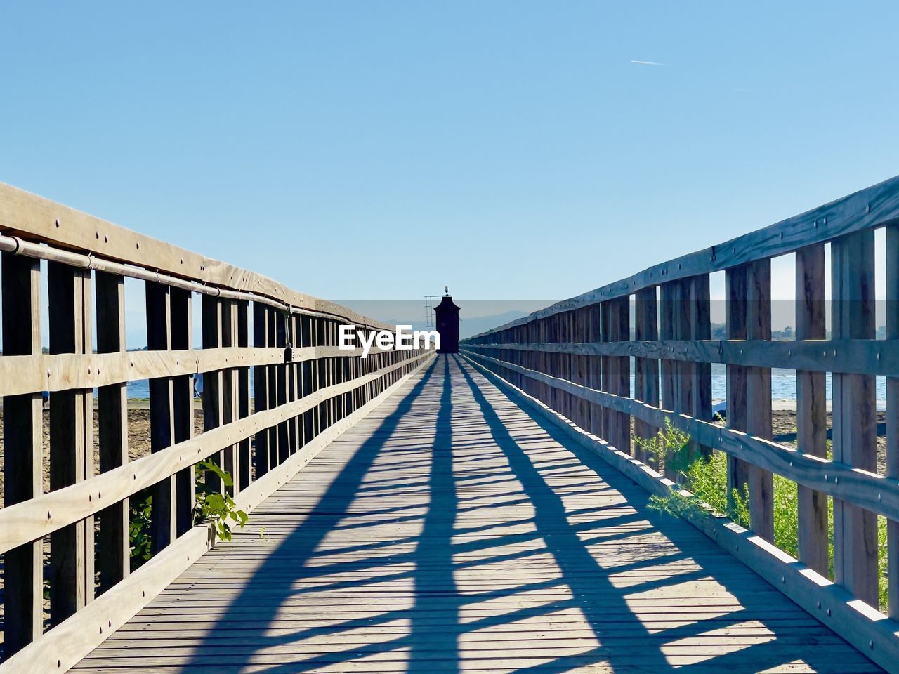 architecture, sky, walkway, one person, built structure, nature, bridge, sunlight, the way forward, clear sky, railing, full length, shadow, sunny, day, adult, footpath, diminishing perspective, footbridge, blue, line, rear view, lifestyles, boardwalk, men, walking, outdoors, transportation, copy space, wood, travel destinations, travel, leisure activity, standing, city