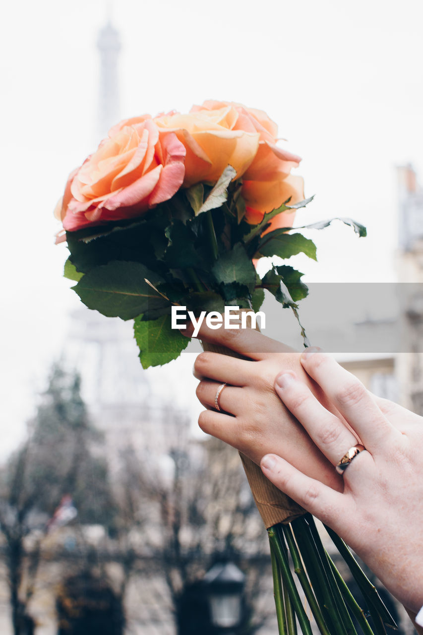 Cropped hand of people holding bouquet against sky
