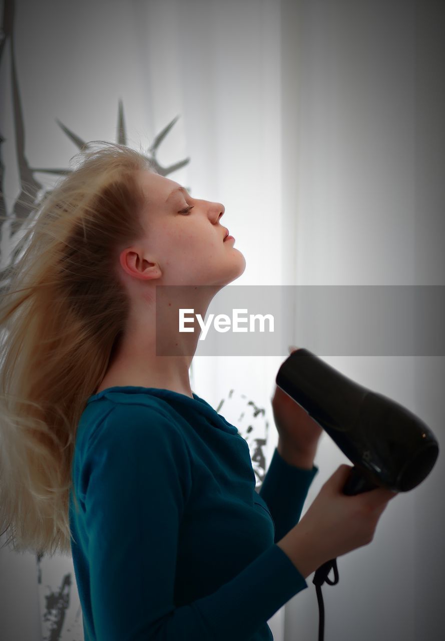 Side view of woman with hair dryer at home