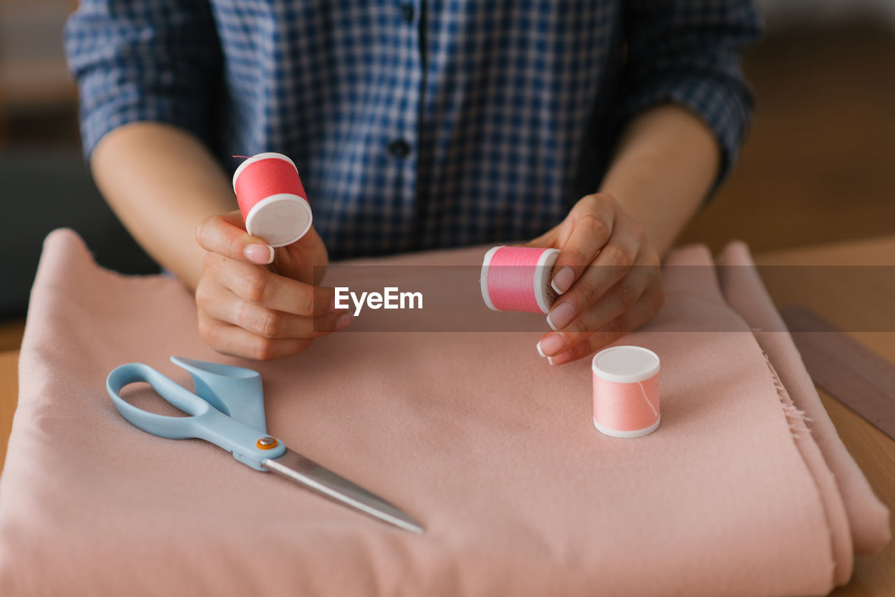 Top view of a dressmaker holding spools of thread near a piece of fabric and scissors