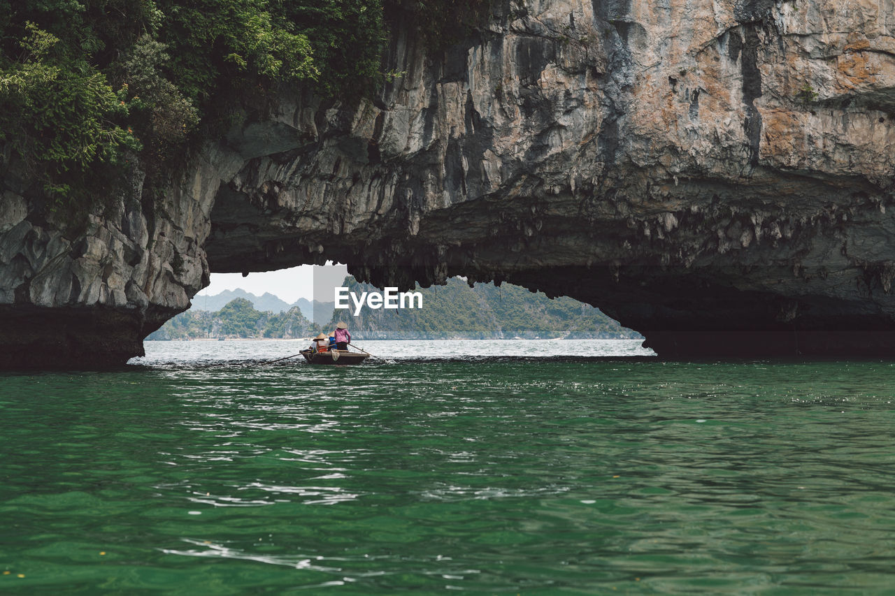 People rowing boat on halong bay under rock formation