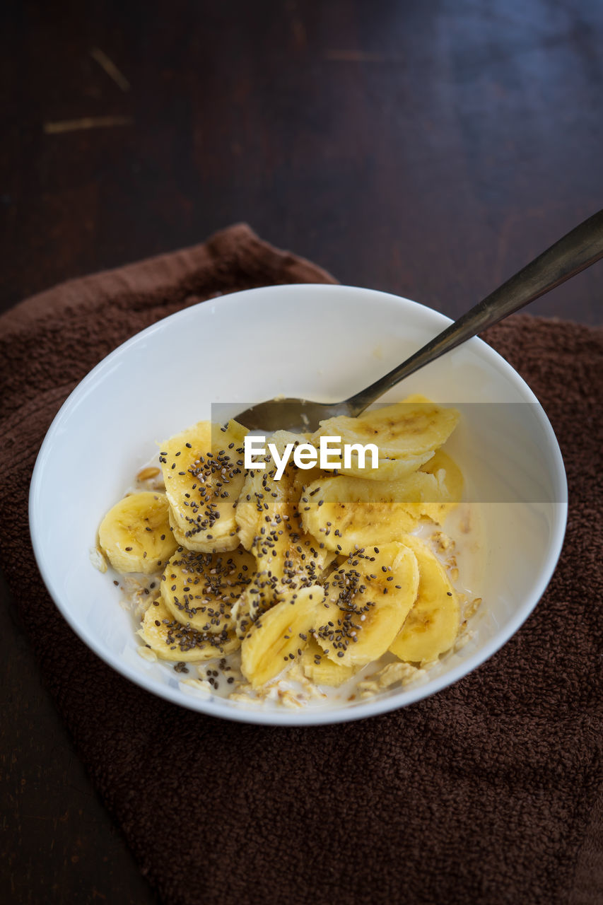 Cereal bowl with slice bananas sprinkled with chia seeds in a bowl on a dark background.