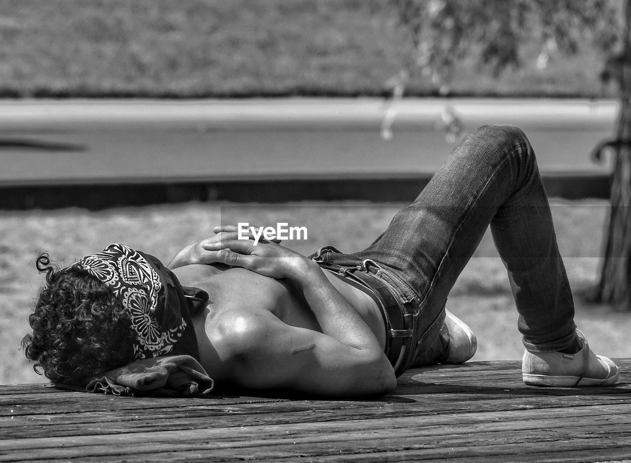 Shirtless man lying on floorboard during summer