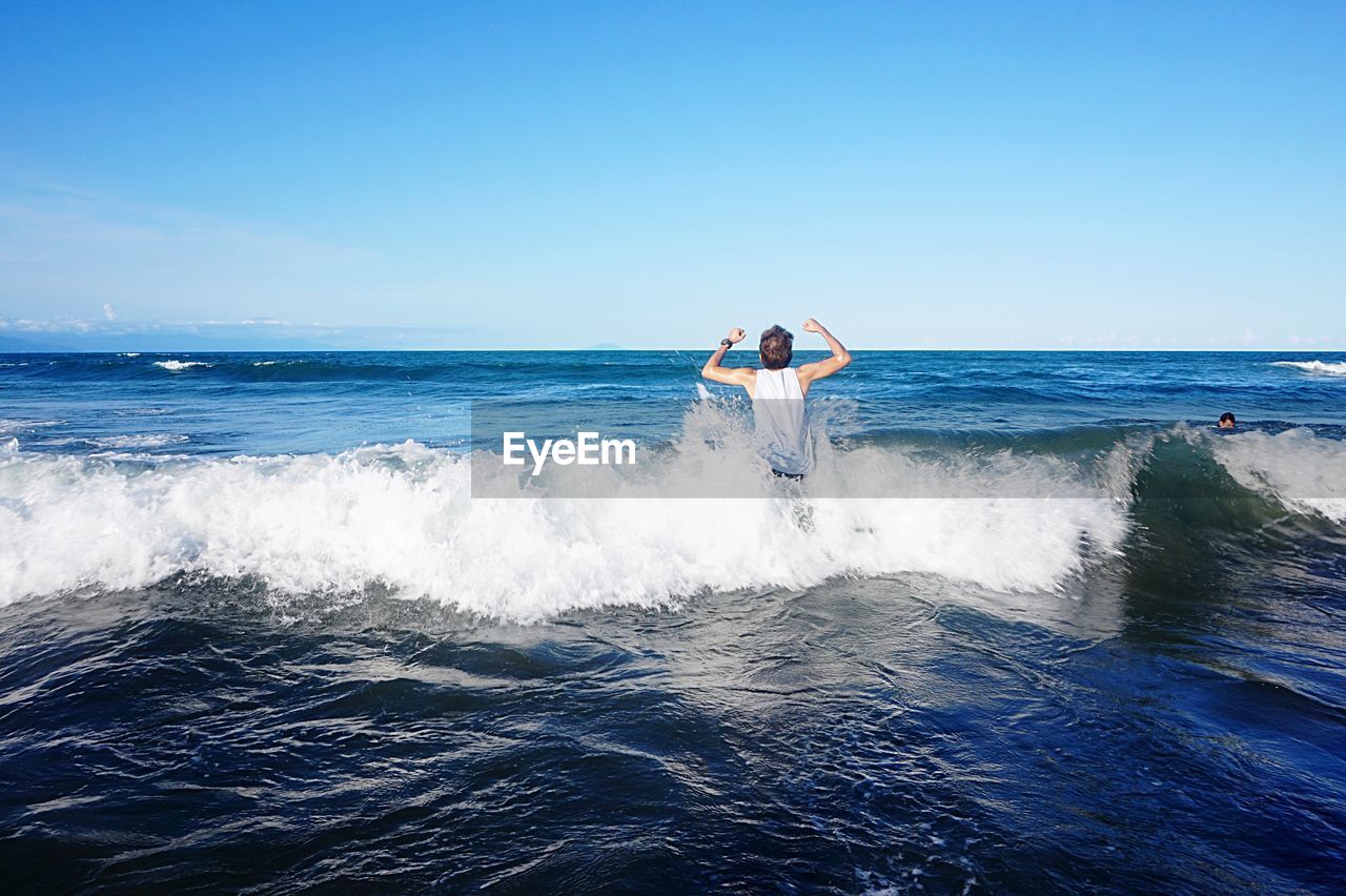 Rear view of man enjoying waves in sea against sky
