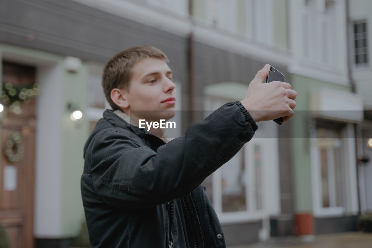 A guy from the millennium generation takes a selfie at every step, holds a mobile smartphone in his 