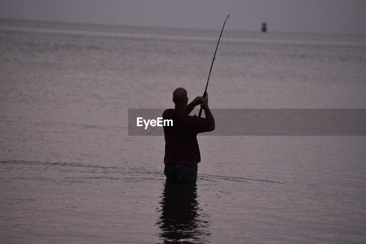 Rear view of fisherman fishing in sea during sunset