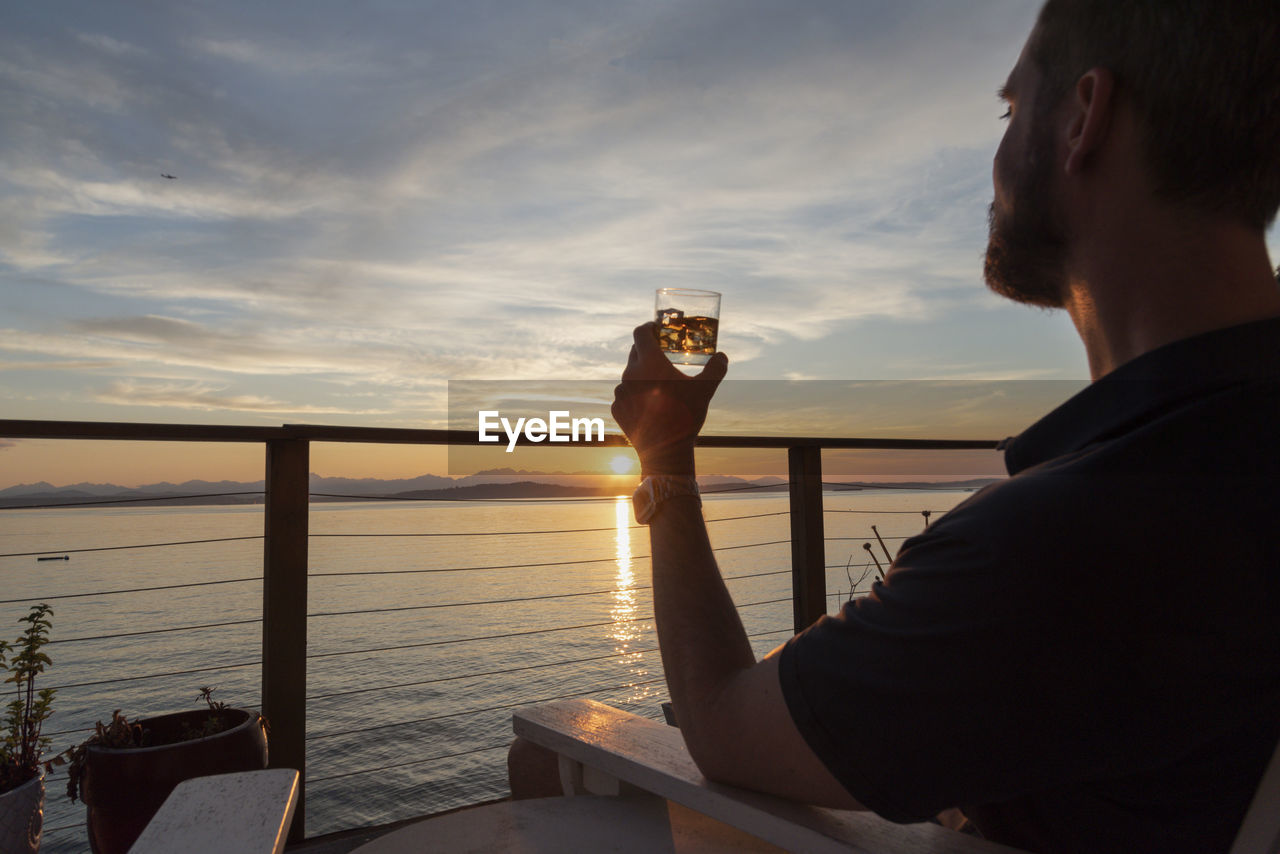 Man with cocktail in hand enjoying sunset from seaside deck.