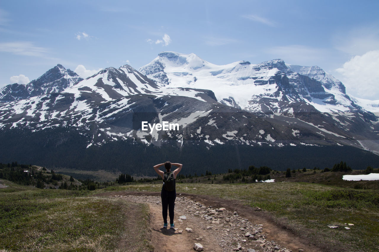 WOMAN STANDING ON SNOWCAPPED MOUNTAINS AGAINST SKY