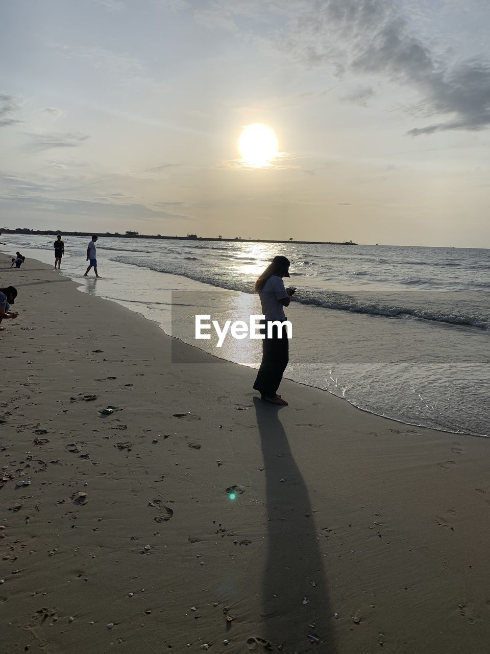 PEOPLE ON BEACH AGAINST SKY AT SUNSET